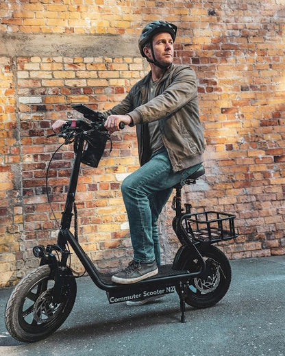 Man riding a seated black electric scooter against a brick wall. Commuter Scooter
